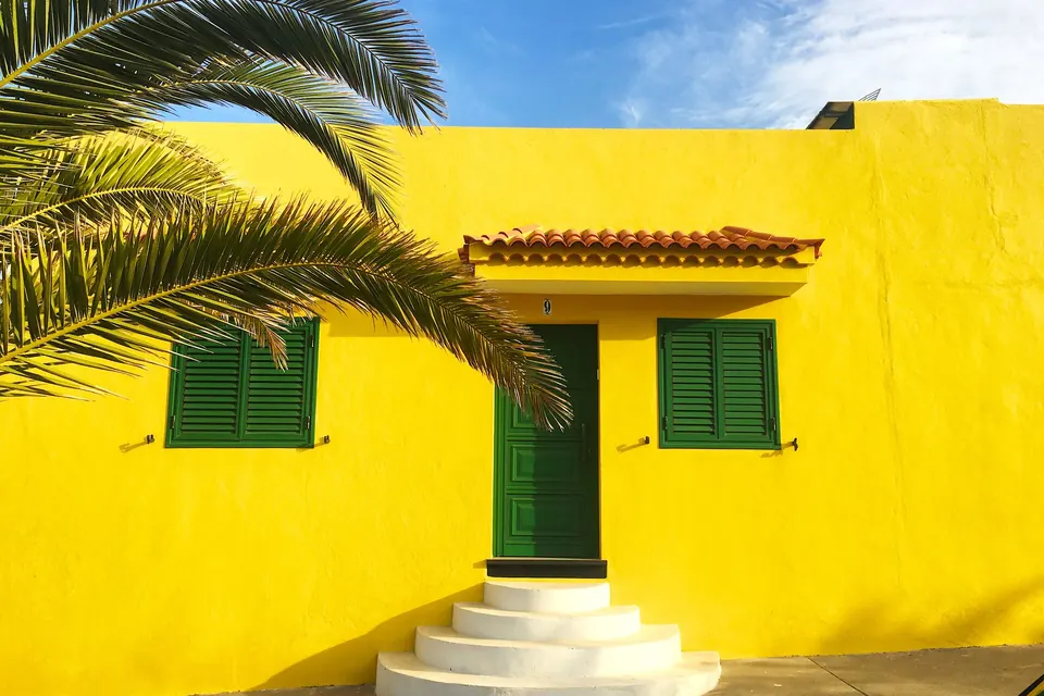 Façade jaune aux volets verts, palmier devant la porte