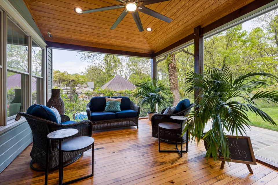 Terrasse couverte au plancher de bois, fauteuils, plantes et brasseur d'air